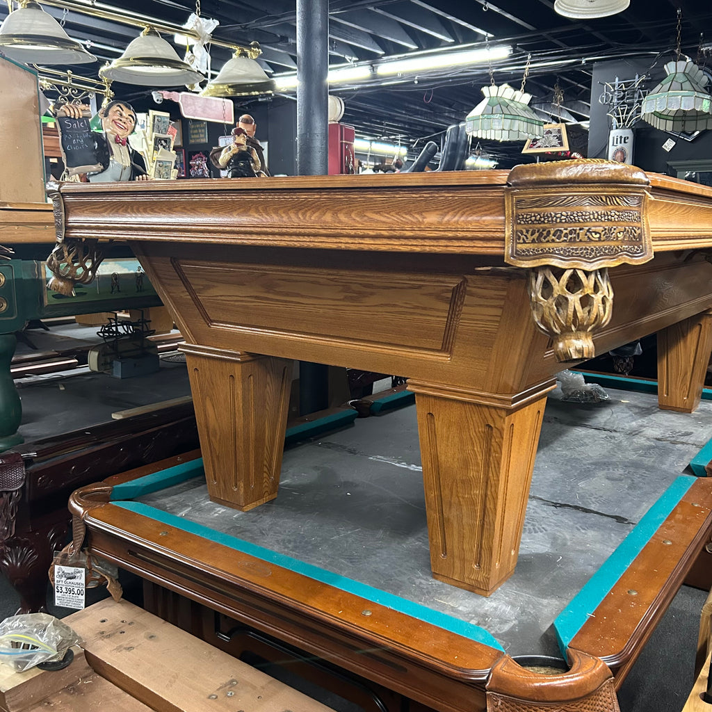 Corner view of pool table with custom leopard shield pocket in oak finish with tapered leg from right side