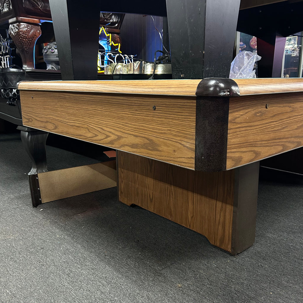 Corner view of oak pool table with brown metal corner caps and pedestal base