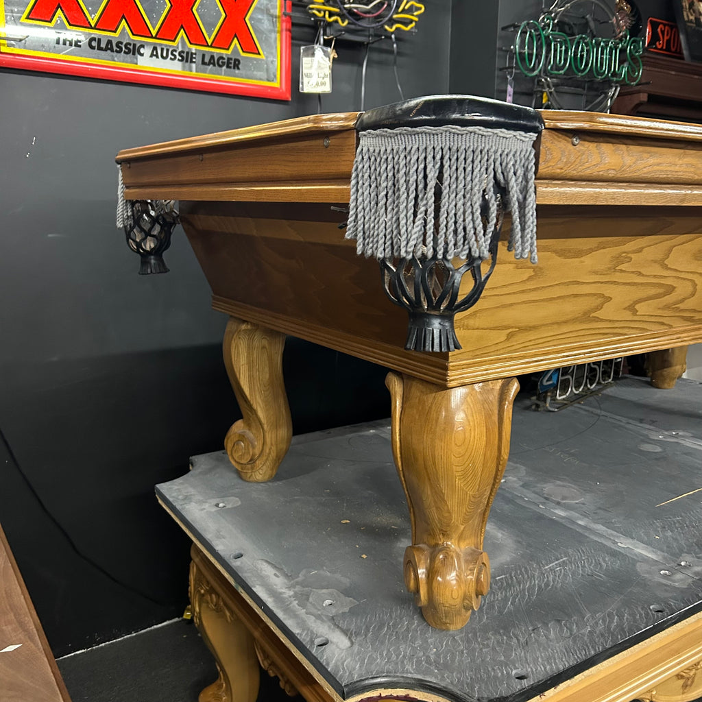 Corner view of pool table in oak finish with fringe pocket with rams horn leg