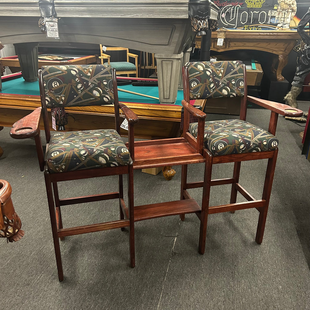 Wooden bar stools with dark 8 ball and cue patterned seats connected with a table