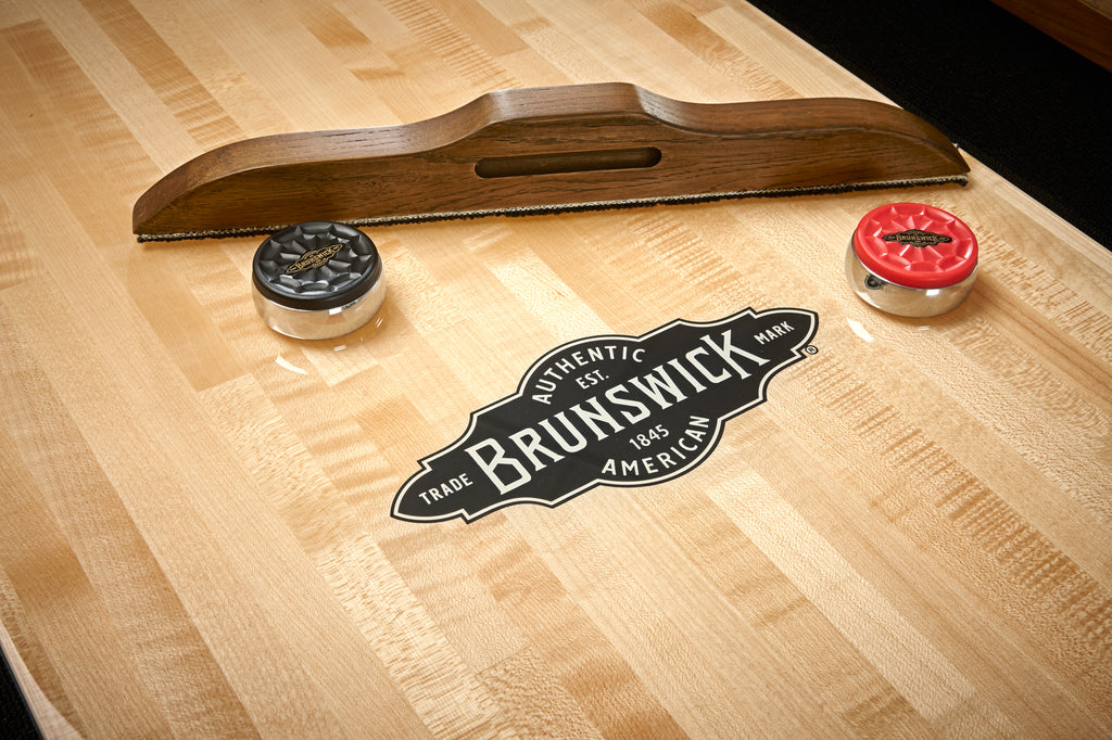 Shuffleboard brush on play surface with red and black puck and brunswick logo